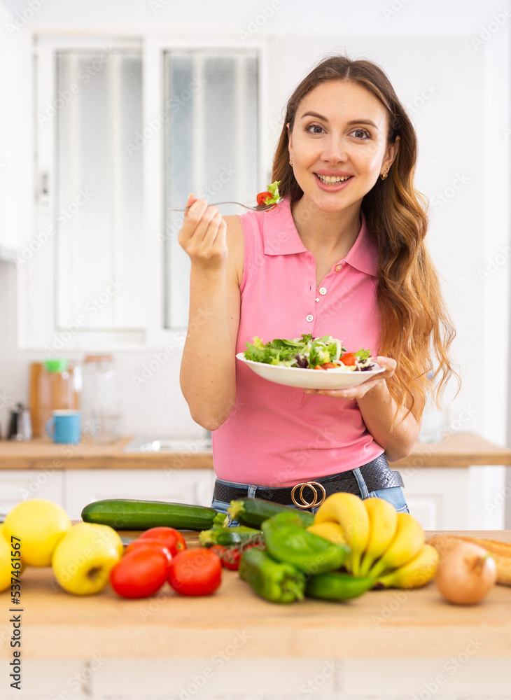 Vegeterian woman standing at table in kitchen and eating vegetable salad Vegeterian woman standing at table in kitchen and eating vegetable salad