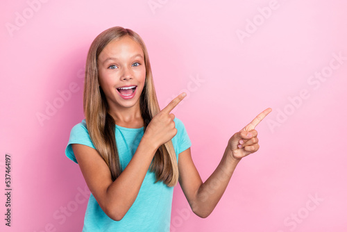 Photo of cheerful positive little child dressed teal t-shirt pointing two fingers empty space isolated pink color background