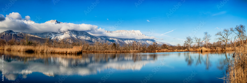 Fototapeta premium Varces et Allières France 11/2021 Etangs du Noiret, jeux de réflexion dans l'eau, reflets des montagnes enneigées, des roseaux et du ciel dans l'étang