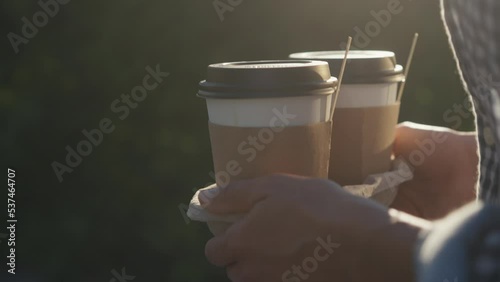 Take-away coffee. Female woman hands holding two paper cups of hot coffee in city summer park.