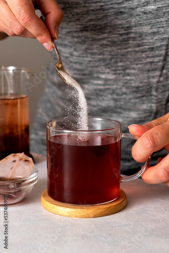 Sugar addiction. Pouring sugar with spoon in cup of tea. Black tea in glass cup. Lifestyle, action drink photo