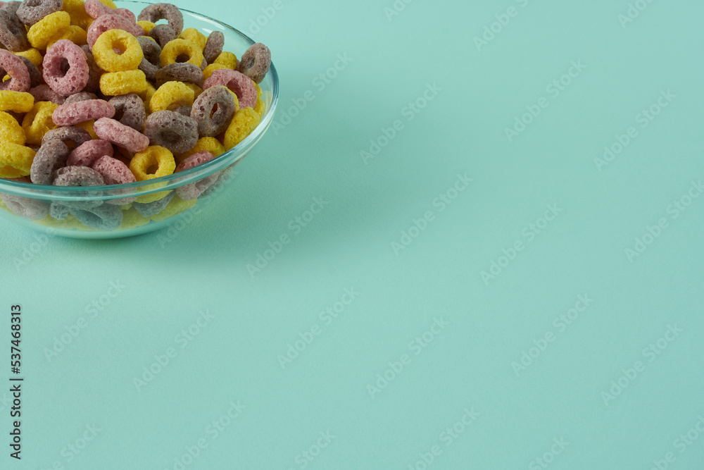 Part of a glass plate with corn rainbow breakfast rings on a turquoise background.