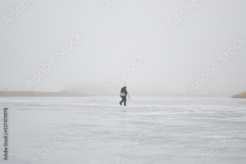 Lonely fisherman on the lake in winter mist