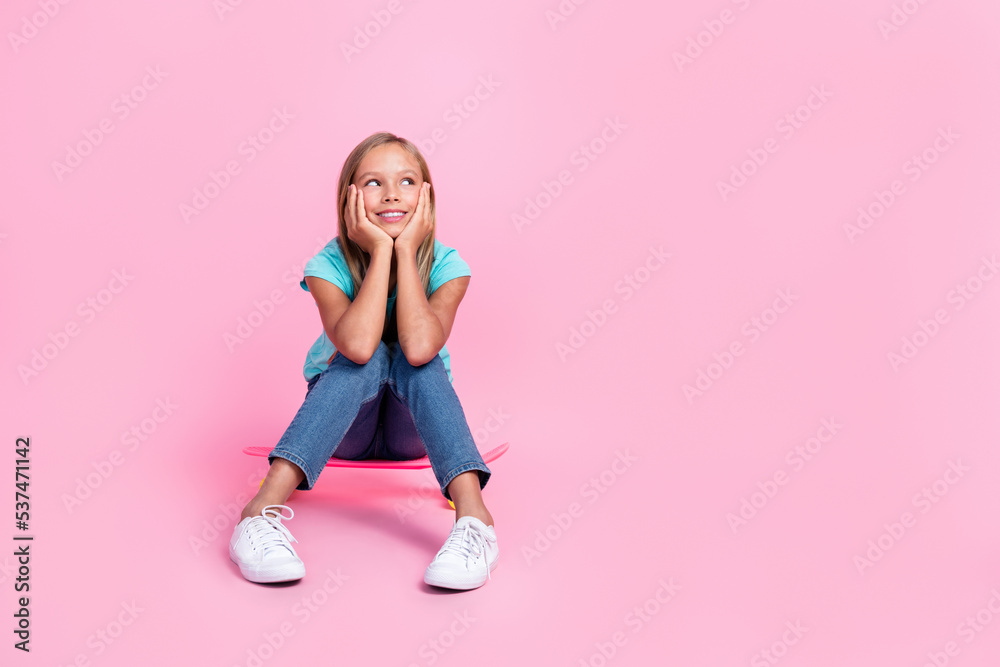 Full length photo of dreamy cute little child dressed teal t-shirt sitting skateboard looking empty space isolated pink color background