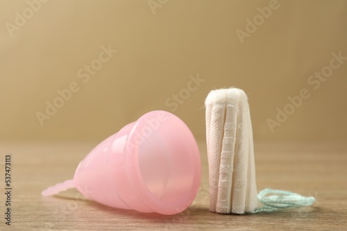 Menstrual cup and tampon on wooden table, closeup photo