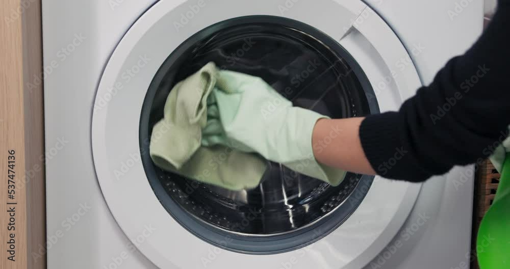 Close-up on the hands of a woman wearing yellow gloves washing the inside of a washing machine drum with a cloth. Close-up on the hands of a woman wearing yellow gloves washing the inside of a washing machine drum with a cloth.