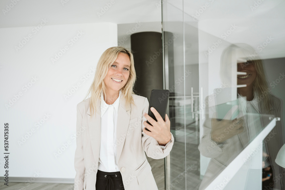 Smiling businesswoman in modern office using mobile phone Smiling businesswoman in modern office using mobile phone