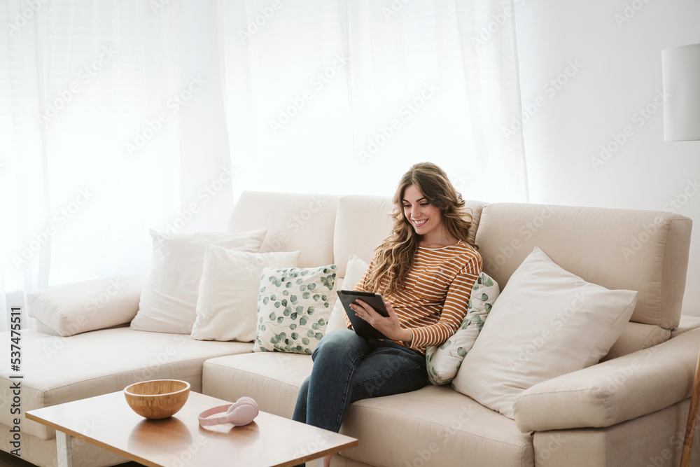 Smiling young woman using digital tablet on sofa at home Smiling young woman using digital tablet on sofa at home