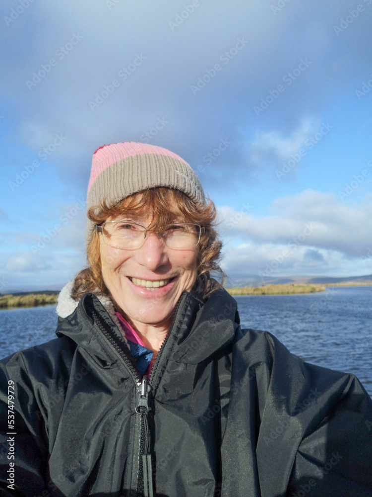 Mature woman taking a selfie after cold water swimming in Keepers Pond - near the summit of the Abergavenny to Bleanavon mountain road. She is wearing a bobble hat and warm weather clothing. Mature woman taking a selfie after cold water swimming in Keepers Pond - near the summit of the Abergavenny to Bleanavon mountain road. She is wearing a bobble hat and warm weather clothing.