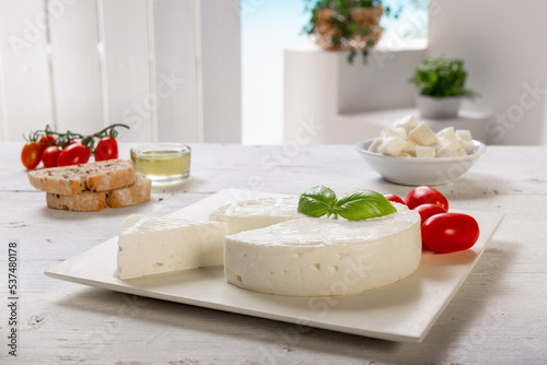 fresh cheese with slice and basil leaf, tomatoes, olive oil, on white square plate, placed on a white wooden table