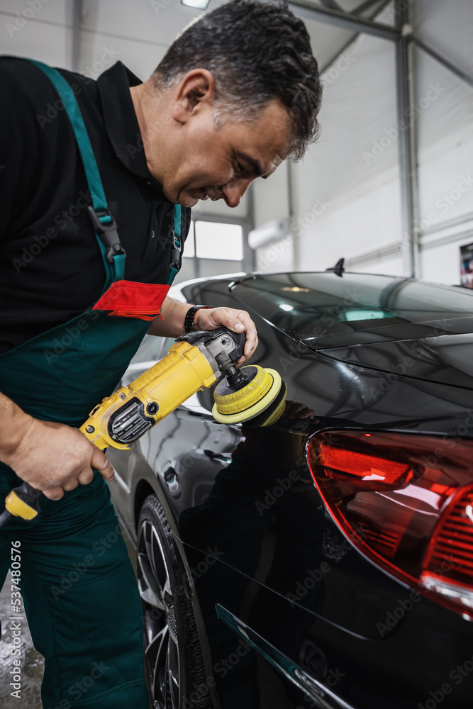 Professional car service worker polishing luxury car with orbital polisher in a car detailing and valeting shop. Ultra wide angle shot. Professional car service worker polishing luxury car with orbital polisher in a car detailing and valeting shop. Ultra wide angle shot.