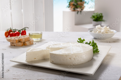 fresh cheese with slice and basil leaf, tomatoes, salad leaf, olive oil, on white square plate, placed on a white wooden table