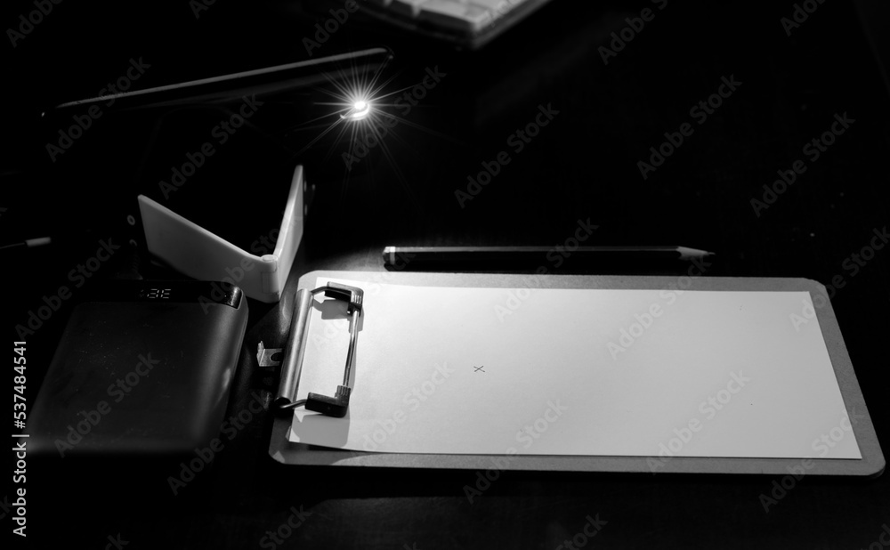 black and white illuminated notepad with mobile and power bank on the desk, energy poverty concept power outages black and white illuminated notepad with mobile and power bank on the desk, energy poverty concept power outages