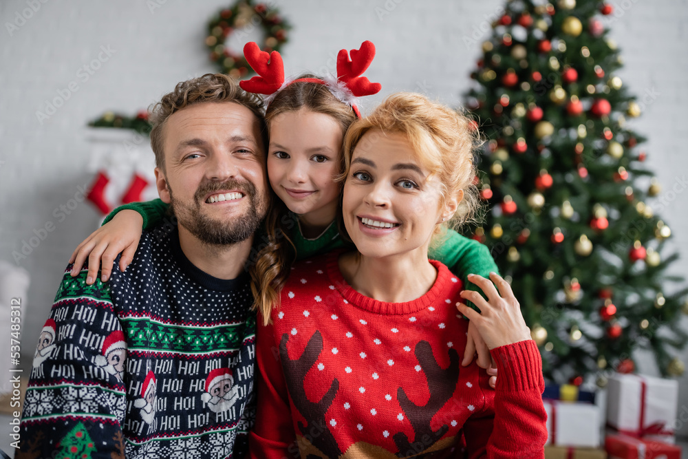 Smiling family in christmas sweaters hugging and looking at camera at home Smiling family in christmas sweaters hugging and looking at camera at home