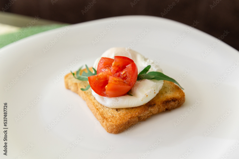 Whole wheat toasted bread with poached egg, tomato, arugula and cheese on white plate.