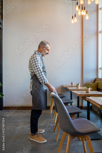 Waiter putting chairs in order in the cafe premises