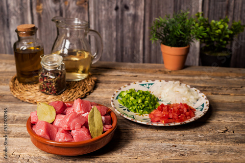 Ingredients for a beef stew, pieces of beef, white wine and chopped vegetables for the stir-fry, on an aged wooden table.