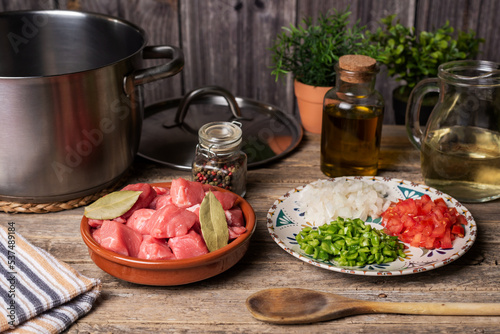 Ingredients next to a pot for a beef stew, pieces of beef, white wine and chopped vegetables for the sauce, on an aged wooden table.