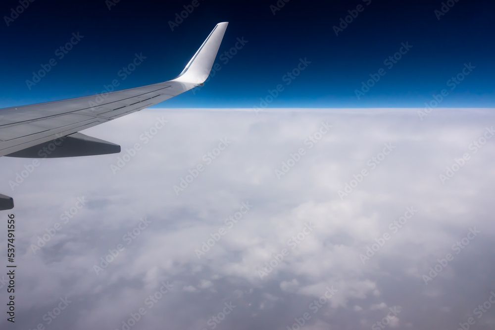 View from the plane window to the wing. Photo taken while flying above the clouds. In the distance, a visible horizon made of clouds View from the plane window to the wing. Photo taken while flying above the clouds. In the distance, a visible horizon made of clouds
