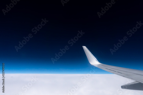 View from the plane window to the wing. Photo taken while flying above the clouds. In the distance, a visible horizon made of clouds