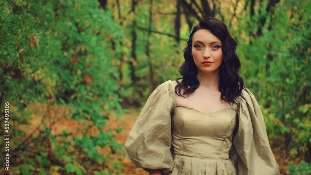 Portrait fantasy woman walks in autumn forest nature. Beauty face evening makeup curly dark hair. Yellow orange foliage on path. Princess girl elf looking at camera. vintage long lush golden dress. Portrait fantasy woman walks in autumn forest nature. Beauty face evening makeup curly dark hair. Yellow orange foliage on path. Princess girl elf looking at camera. vintage long lush golden dress.