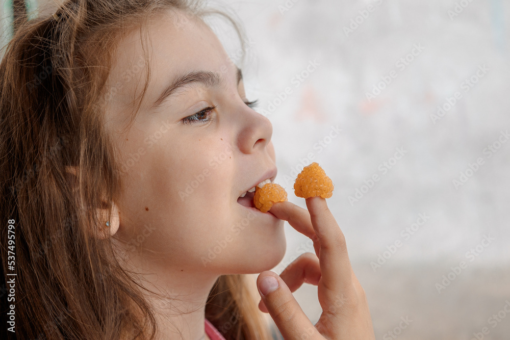 Young girl is holding yellow raspberries on her fingers and tasting. High quality photo Young girl is holding yellow raspberries on her fingers and tasting. High quality photo