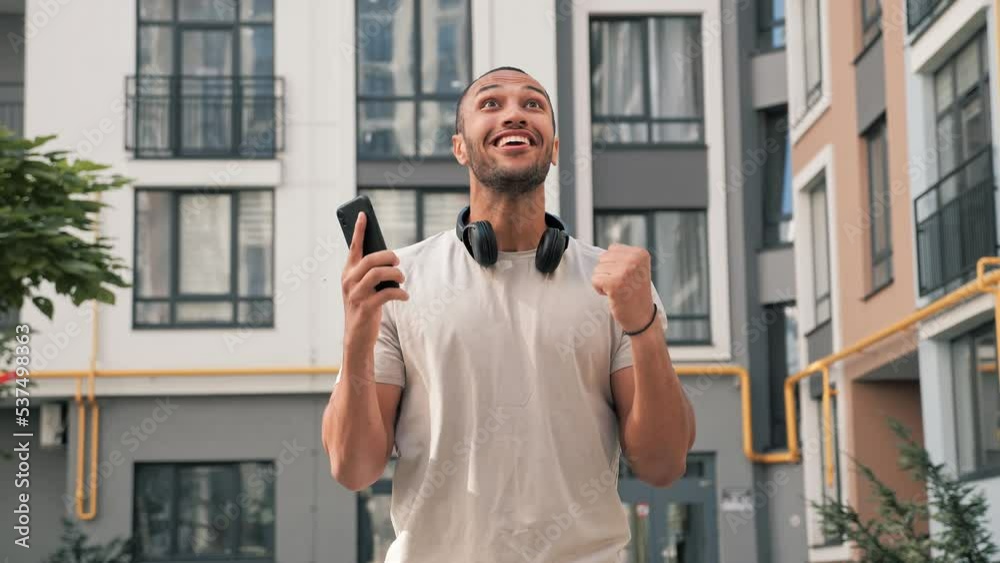 Excited african american man standing outdoors reading email on phone with good news receiving great offer job promotion winning lottery receives cash prize celebrating victory rejoicing in success.
