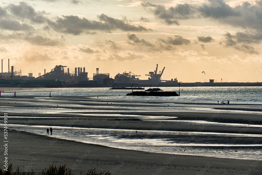 Fototapeta premium low tide and a steelworks in silhouette and port with loading cranes and containers of the port of Dunkirk, France