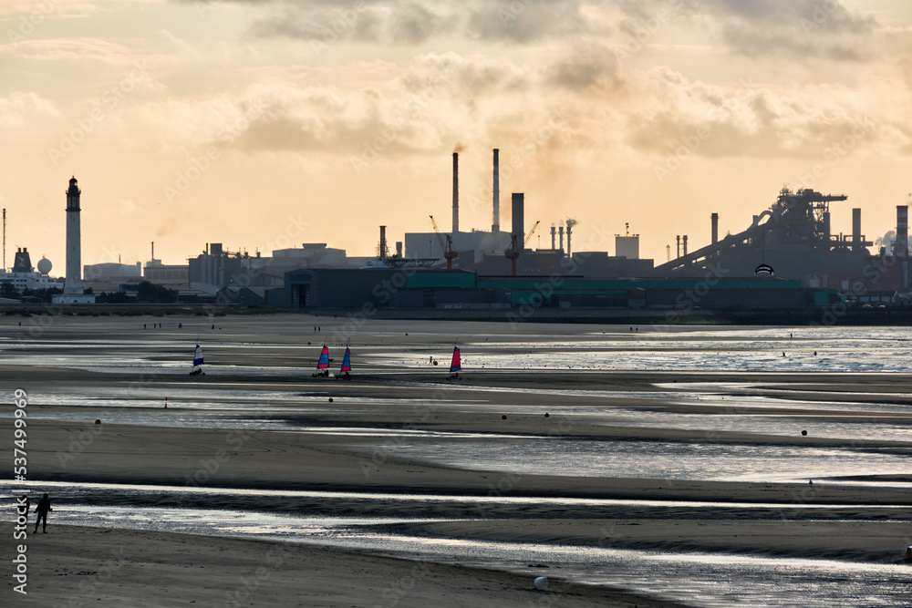low tide and a steelworks in silhouette and port with loading cranes and containers of the port of Dunkirk, France low tide and a steelworks in silhouette and port with loading cranes and containers of the port of Dunkirk, France