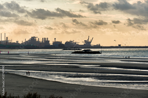 low tide and a steelworks in silhouette and port with loading cranes and containers of the port of Dunkirk, France