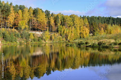 the reflection of yellow-green trees on the steep banks of the river on a sunny day in autumn