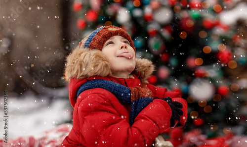 Child catch snowflakes with tongue. Christmas and New Year tree cozy. Concept of childhood and happiness. New Year Christmas holiday. Happy kid playing with snow outdoor. Holidays winter season.