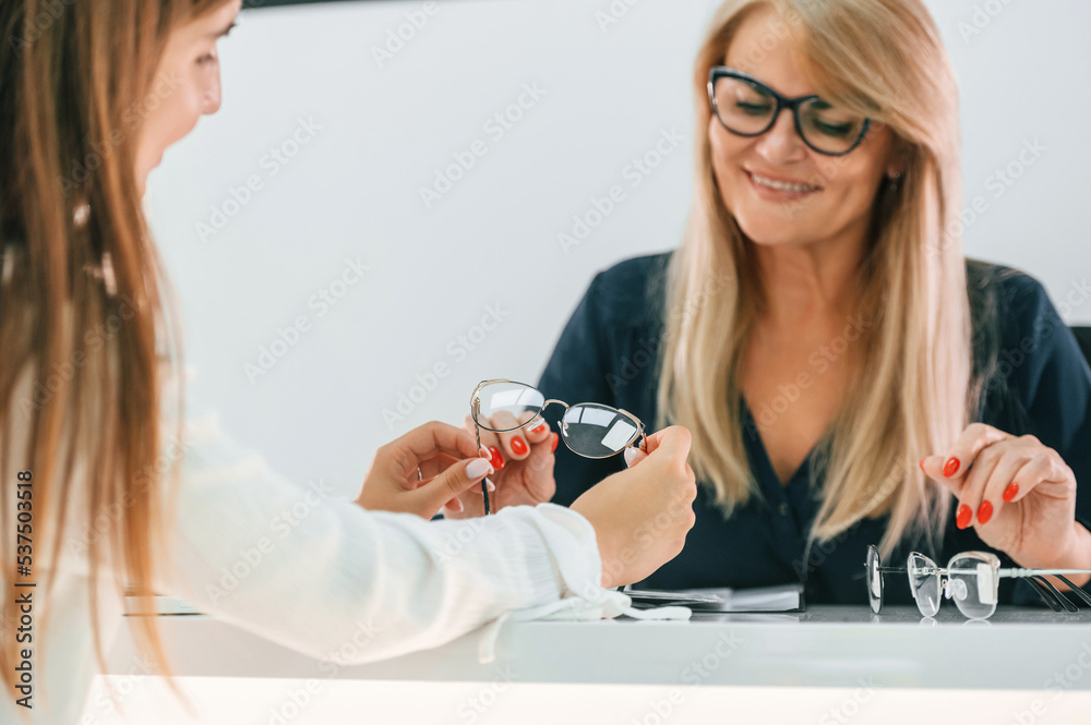 Sitting and looking for a new glasses. Woman is in the store getting help by assistant