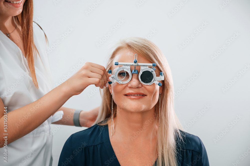 Wearing glasses. Woman's vision is tested by clinic worker that using special device Wearing glasses. Woman's vision is tested by clinic worker that using special device