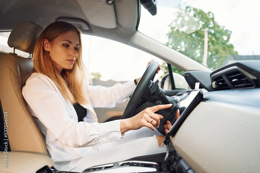 Navigating the vehicle's interface. Young woman in white clothes is with her electric car at daytime