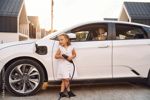 Having fun. Little girl standing near electric car with charging cable in hands © standret