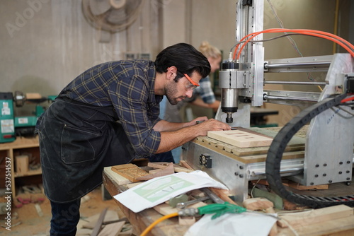 Contemporary Carpenter Working, Portrait of modern carpenter making wood furniture while working in joinery lit by sunlight with factory background on small business concept, copy space © FotoArtist