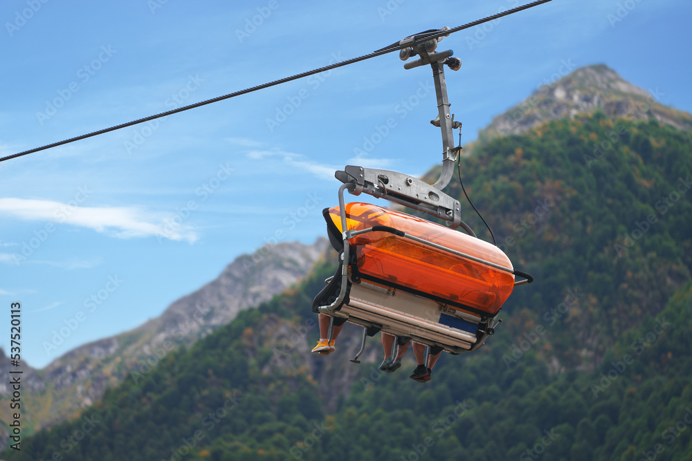 A four-seat cable chairlift with passengers at a height against the background of a mountain. Copy space. A four-seat cable chairlift with passengers at a height against the background of a mountain. Copy space.