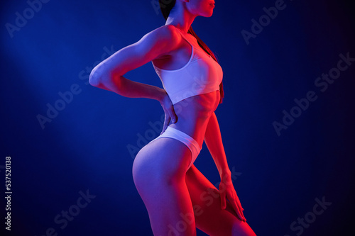 Side view. Young woman in underwear is in the studio with neon lights