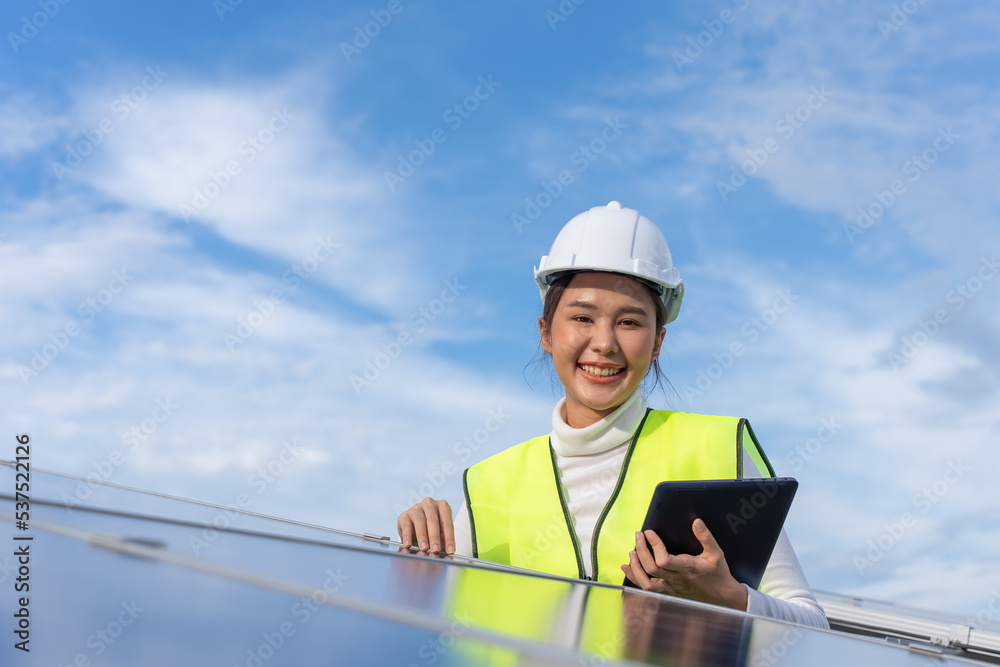 Fototapeta premium Beautiful Asian female engineer uses a black tablet to inspect solar power station, Clean energy.