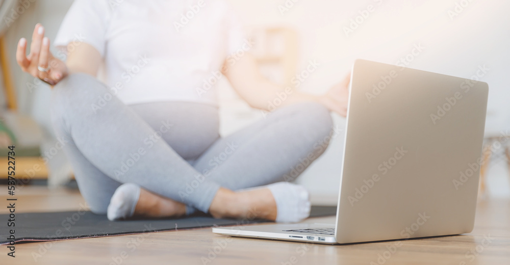Naklejka premium Young pregnant woman practicing online yoga at home with laptop, banner lifestyle pregnancy concept