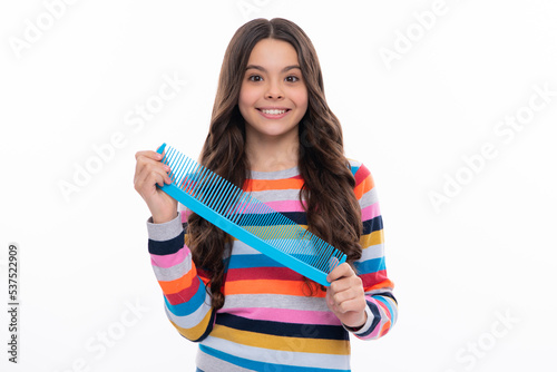 Teenager brushing combing hair with big comb on yellow isolated studio background. Teen girl with hairbrush. Kids hairstyle. Happy girl face, positive and smiling emotions.