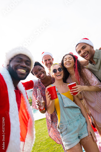 Portrait of diverse friends with santa hats in garden at christmas