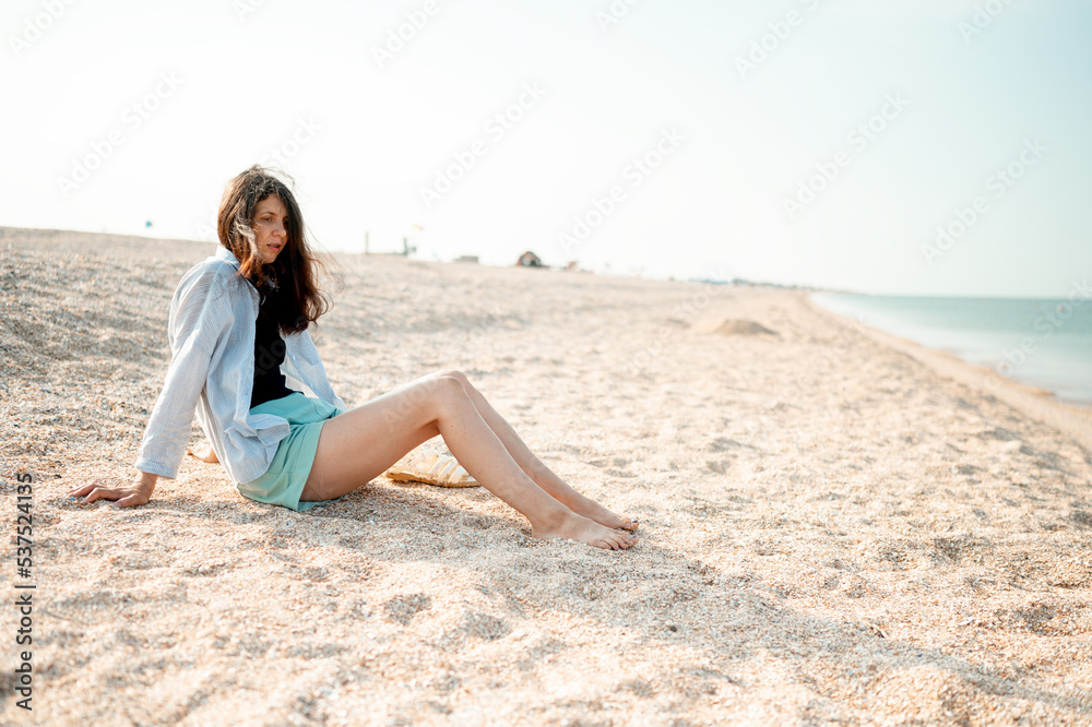 Beautiful young girl with long hair sits on the seashore and enjoys the sea air