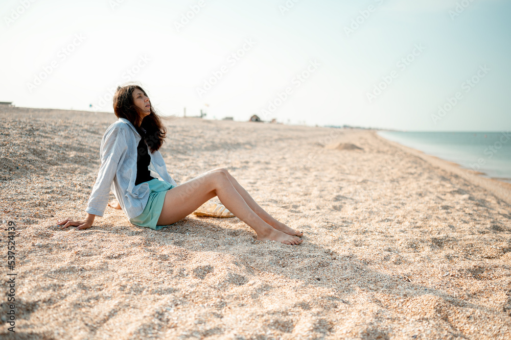 Beautiful young girl with long hair sits on the seashore and enjoys the sea air Beautiful young girl with long hair sits on the seashore and enjoys the sea air