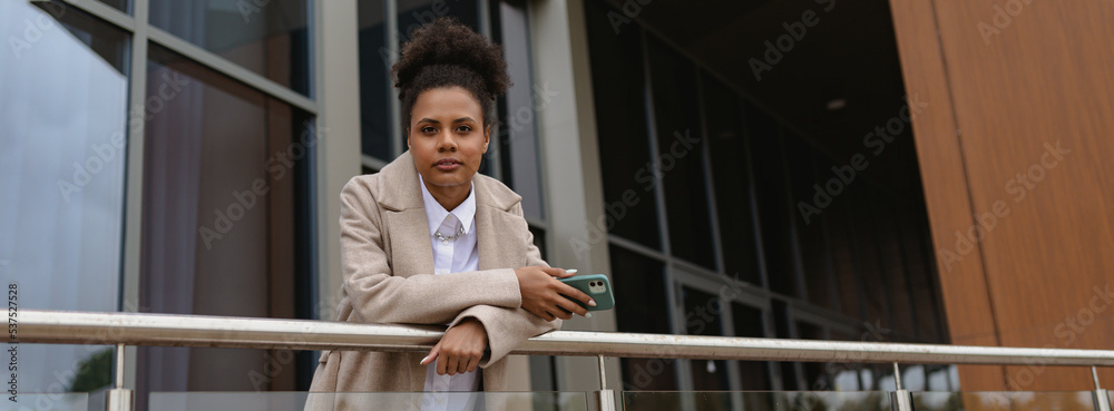 serious business african american woman in business clothes on the background of an office building looks at the camera