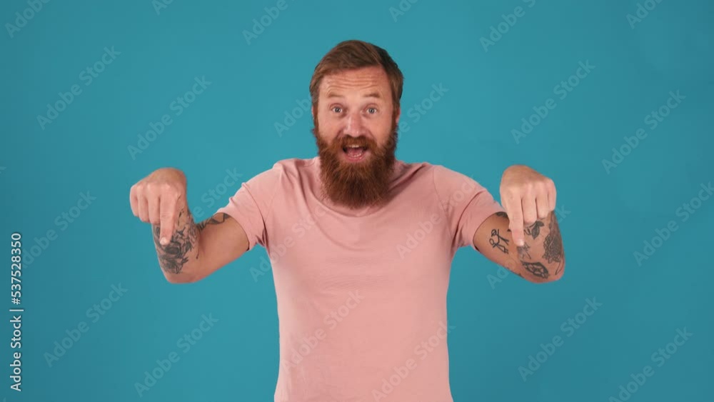 Smiling man waving hand and pointing down at the camera in the blue studio Smiling man waving hand and pointing down at the camera in the blue studio