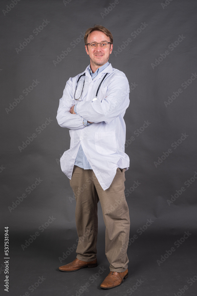 Full length shot of male doctor with stethoscope over neck in medical coat against gray background Full length shot of male doctor with stethoscope over neck in medical coat against gray background