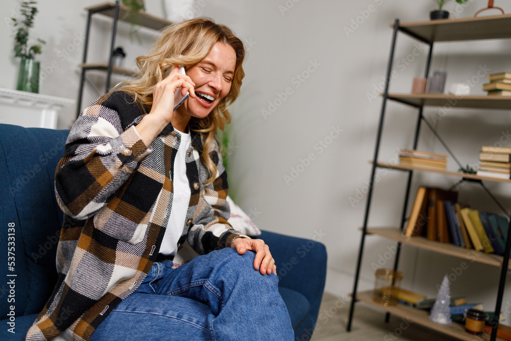 Joyful woman talking on the phone and laughing while sitting on the sofa at home Joyful woman talking on the phone and laughing while sitting on the sofa at home