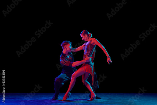 Two dancing people, ballroom dancers in elegance outfits in motion, action over dark background in neon light. Concept of art, music, dance, emotions. © master1305